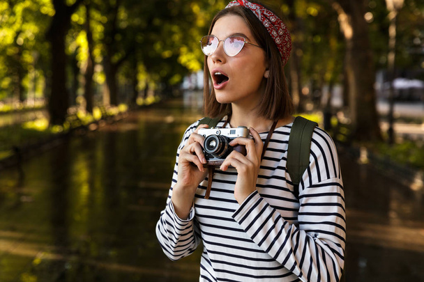Image of excited shocked young beautiful woman walking outdoors with camera. - Photo, Image