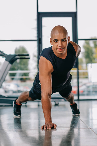 african american sportsman looking at camera and doing push ups on one hand at gym - Foto, Bild