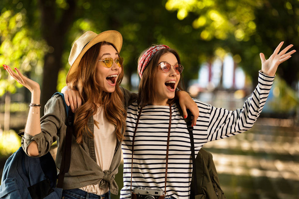 Image of excited pretty young happy women friends walking outdoors with backpacks hugging. - Valokuva, kuva