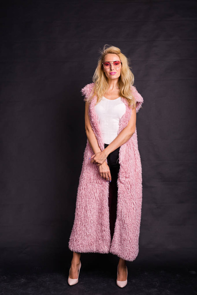 Концепция моды и людей - молодая блондинка в очках, стоящая в розовой шубе и улыбающаяся
 - Фото, изображение