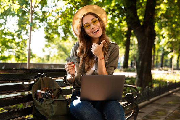 Photo of young beautiful excited happy woman outdoors sitting using laptop computer make thumbs up. - Foto, Imagem