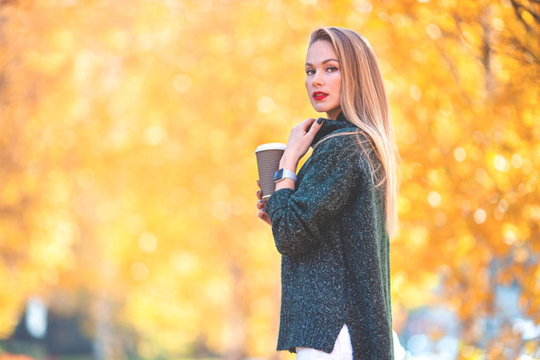 Jesienna koncepcja - piękna kobieta pijąca kawę w jesiennym parku pod jesiennymi liśćmi - Zdjęcie, obraz