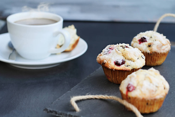 Cranberry Muffins on a slate serving tray with open muffin with butter and a steaming hot cup of coffee in the background. Extreme shallow depth of field with selective focus on center muffin.  - Foto, imagen