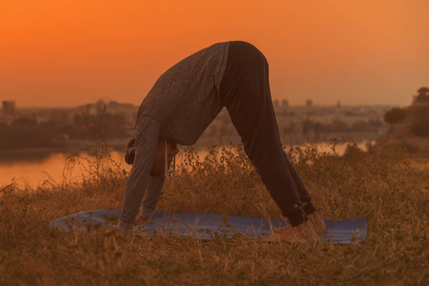 Homem fazendo ioga no pôr do sol com vista para a cidade, Adho Mukha Svanasana / Downward enfrentando cão pose.Toned imagem
. - Foto, Imagem