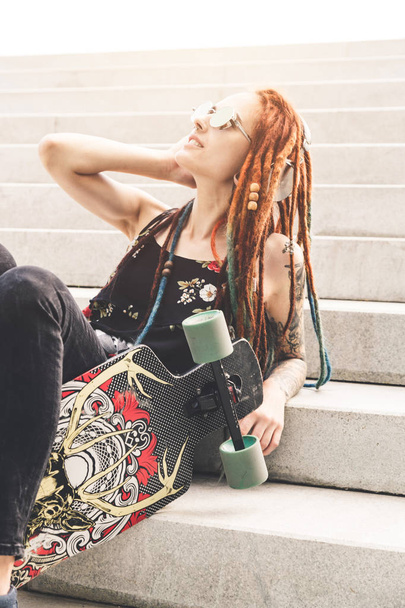 UFA, RUSSIA - September 12, 2018 Editorial photo of young girl with tattoo and dreadlocks listening to music while sitting on the steps - Φωτογραφία, εικόνα