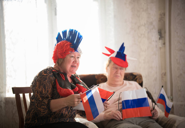 Pastimes. An elderly women supports sport team sitting against TV on the backgrond of window - Fotografie, Obrázek