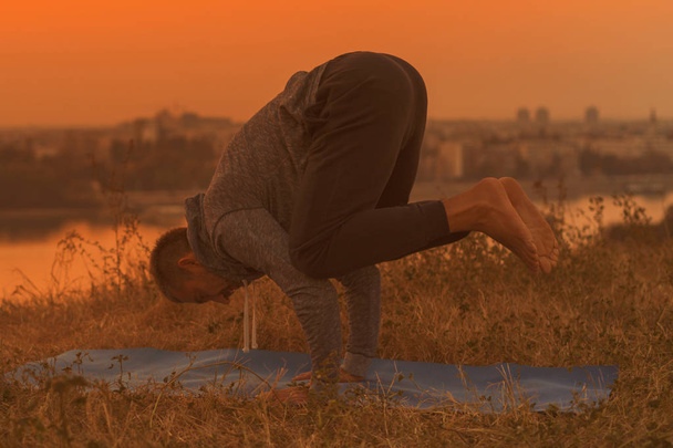Mann macht Yoga bei Sonnenuntergang mit Blick auf die Stadt, Bakasana / Kranichpose.getöntes Bild. - Foto, Bild