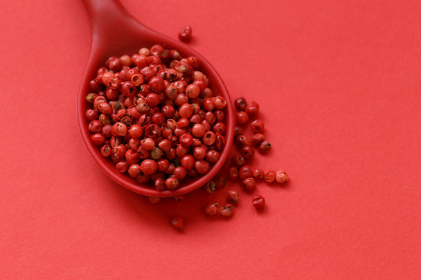 roze peper erwten in een lepel op een rode achtergrond - Foto, afbeelding
