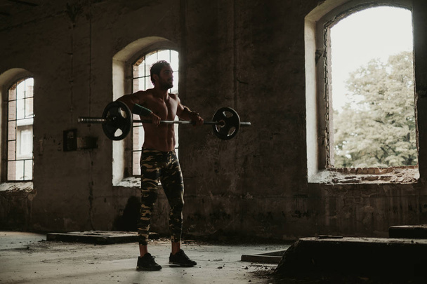 Focused male athlete doing clean and jerk in an old building in the middle of the day - Photo, Image