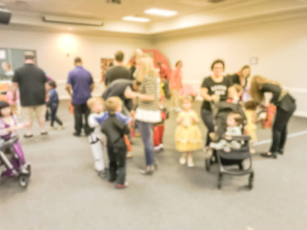 Motion blurred kids and parents with strollers enjoy indoor Halloween party at school in Texas, America. Defocused children with costumes at fall fun games - Photo, Image