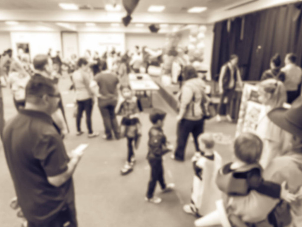 Vintage tone blurred abstract kids and parents enjoy indoor Halloween party at school in Texas, America. Defocused children with costumes at fall fun games, shape links - Photo, Image