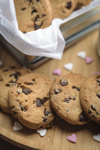 Biscotti con gocce di cioccolato su un piatto di legno e in una piccola scatola decorata con cuori di zucchero. Concetto Valentine
. - Foto, immagini