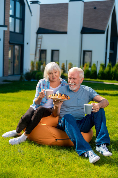Elderly wife and husband feeling relaxed having tea time outside summer house - Foto, Imagem