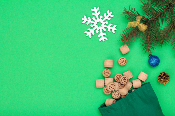Board game lotto. Wooden lotto barrels with bag for a game in lotto, Christmas fir tree branche and cone on green background. Top view - Fotografie, Obrázek