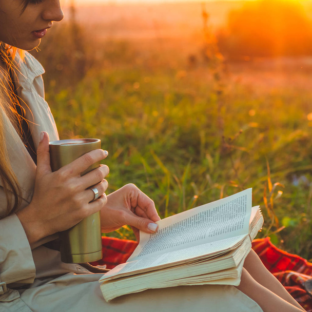 Käsite elämäntapa ulkona virkistys syksyllä. Hattupäinen tyttö luki ruudullisia kirjoja lämpökupillisella. Syksyllä. Auringonlasku. Kodikas
 - Valokuva, kuva