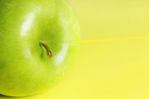 Green apple still life on a yellow background ,front view , reflections on the apple surface ,bright colors , selective focus  ,a yellow and out of focus line in the background - Zdjęcie, obraz