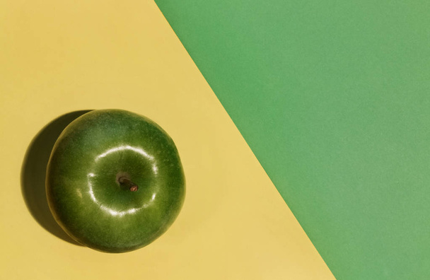 One green apple on a yellow and green background , top view , studio shot ,a small  apple shadow on the background - Zdjęcie, obraz