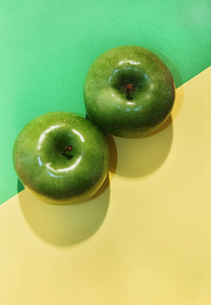 Two beautiful green apples on a yellow and green background ,studio shot , top view ,apple shadow  on the background - Foto, imagen