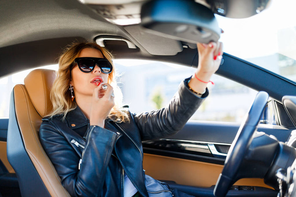 Bild einer jungen Frau mit schwarzer Brille bemalt Lippen im Auto - Foto, Bild