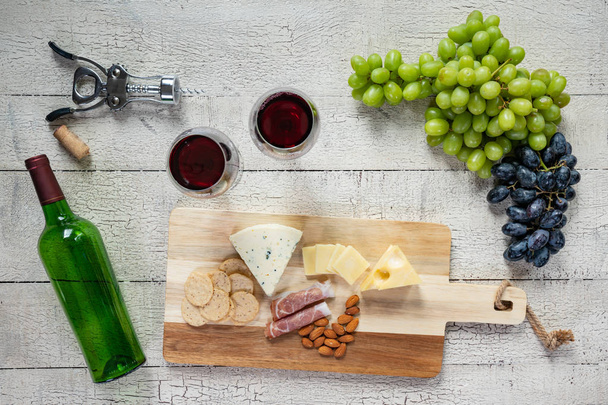 Kieliszek czerwonego wina z butelki wina, sery, krakersy, szynka, migdały i winogron - Zdjęcie, obraz