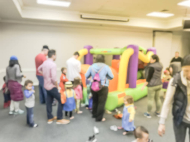 Motion blurred diverse multiethnic children enjoy inflatable bounce house jumping game. Defocused parents and kids at indoor school Halloween party in Texas, America - Photo, Image