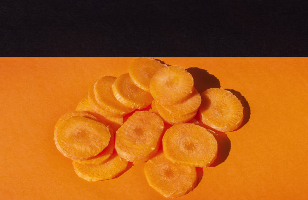 A beautiful bunch of sliced carrots on a colored background   ,top view ,studio shot , orange and black color harmony - Zdjęcie, obraz