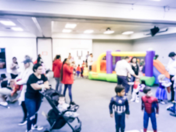 Abstract blurred diverse multiethnic children enjoy inflatable bounce house jumping game. Defocused parents and kids with stroller at indoor school Halloween party in Texas, America - Photo, Image