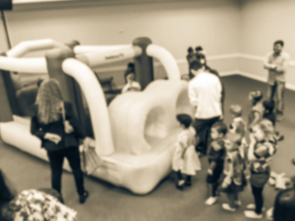 Винтажный тон абстрактные размытые разнообразные многоэтнические дети пользуются надувные надувной дом прыжки игры. Отстраненные родители и дети на вечеринке в честь Хэллоуина в Техасе, Америка
 - Фото, изображение
