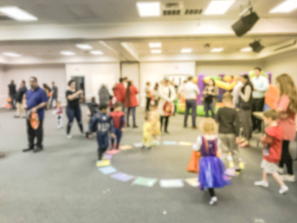 Homályos mozgás sokrétű soknemzetiségű gyermekek élvezze kör játék, Texas, Amerikai. Defocused szülők és a gyerekek iskolai fedett Halloween Party. - Fotó, kép