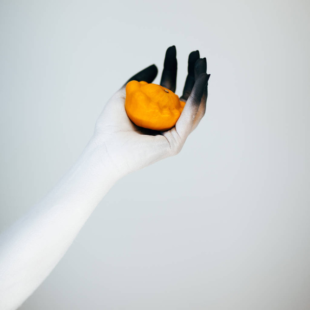 Creepy Halloween monster hand with white and black make up holding little pumpkin in front of white background - Fotoğraf, Görsel