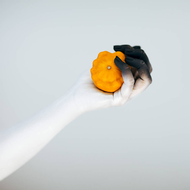 Creepy Halloween monster hand with white and black make up holding little pumpkin in front of white background - Foto, Bild