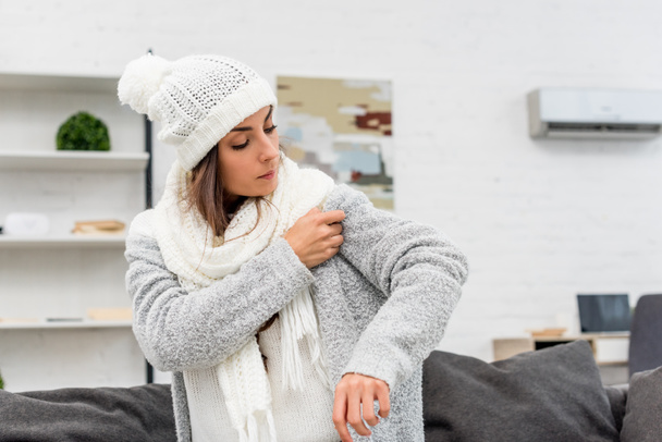 freezed young woman putting on warm clothes with air condition hanging on background - Foto, Imagen