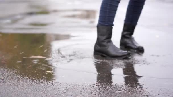 dívka v černé kožené boty klopýtá v podzimní louži po dešti. - Záběry, video