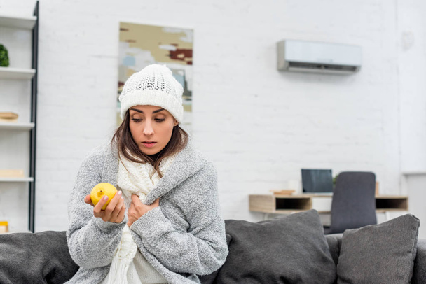 хвора молода жінка в теплому одязі тримає лимон вдома
 - Фото, зображення