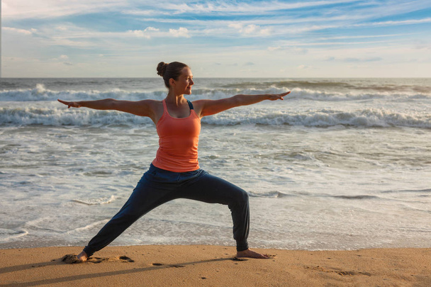 Frau macht Yoga Asana Virabhadrasana 1 Krieger posieren am Strand auf - Foto, Bild