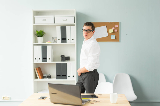 Business, bureau, concept de personnes - bel homme à lunettes se tient dans le bureau près d'un ordinateur et souriant
 - Photo, image