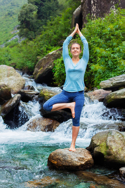 Woman in yoga asana Vrikshasana tree pose at waterfall outdoors - Photo, Image