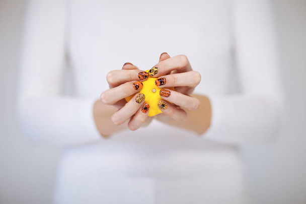 Beautiful woman hands with cute halloween nail polish holding little pumpkin - Zdjęcie, obraz