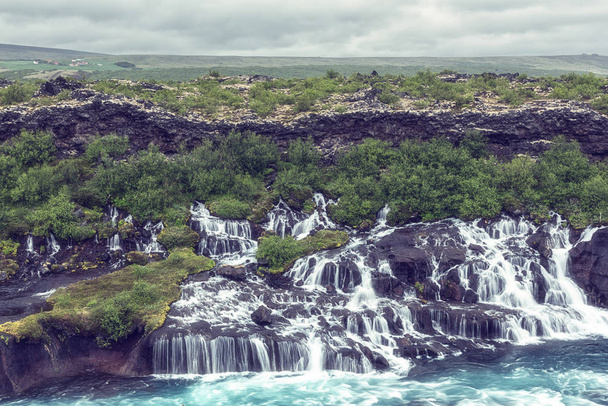 Hraunfossar watervallen of Lava Falls, IJsland. Mooie zomerse landschap, water stroomt door de lava rotsen in de rivier van de emerald gekleurde Hvita. Een van de meest ongewone watervallen in IJsland - Foto, afbeelding