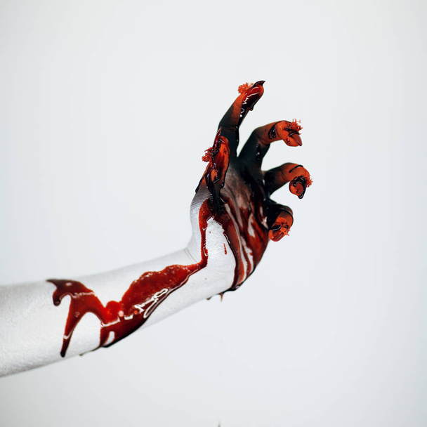 Creepy bloody horror Halloween monster witch hand with white, red and black make up and long creepy fingernails in front of white background - Fotó, kép