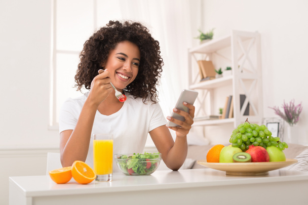 Афро-американської жінкою, їдять здорову салат і за допомогою смартфона - Фото, зображення