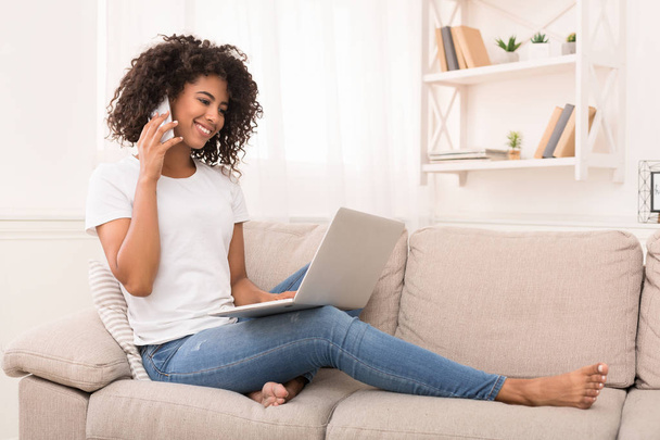 Confident african-american girl using laptop and talking on smartphone - Foto, immagini