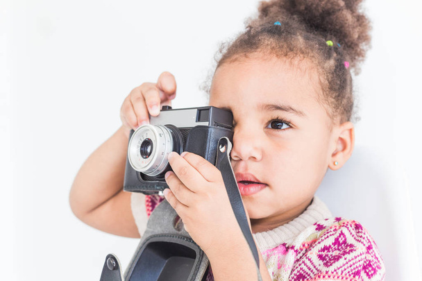 Portrait of a little girl in a colorful dress taking pictures on an old vintage camera - Foto, Imagen