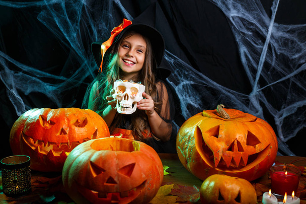 Halloween Witch concept - little witch child with halloween sweet and candy with cheerful smiling over spider web and with curved pumpkins background. - Fotoğraf, Görsel