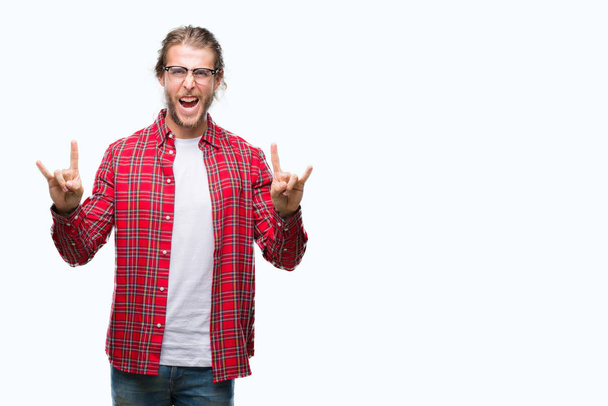 Young handsome man with long hair wearing glasses over isolated background shouting with crazy expression doing rock symbol with hands up. Music star. Heavy concept. - Foto, Imagem