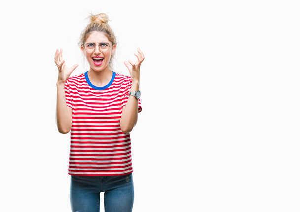 Young beautiful blonde woman wearing glasses over isolated background crazy and mad shouting and yelling with aggressive expression and arms raised. Frustration concept. - Photo, Image
