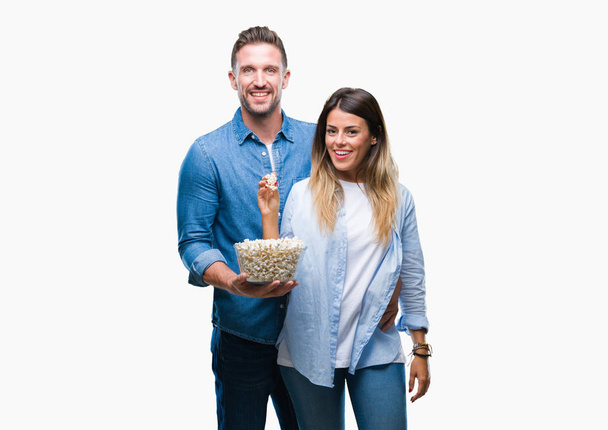 Jovem casal apaixonado comer pipocas sobre fundo isolado com um rosto feliz de pé e sorrindo com um sorriso confiante mostrando dentes
 - Foto, Imagem
