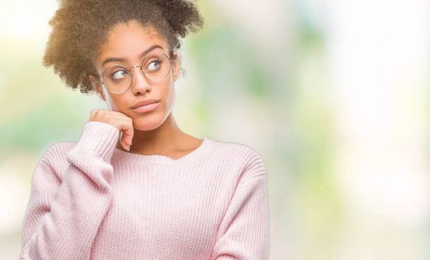 Jonge afro-Amerikaanse vrouw dragen bril over geïsoleerde achtergrond met hand op kin denken over de vraag, nadenkend expressie. Glimlachend met doordachte gezicht. Twijfel concept. - Foto, afbeelding