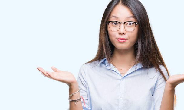 Jeune femme d'affaires asiatique portant des lunettes sur fond isolé expression désemparée et confuse avec les bras et les mains levées. Concept de doute
. - Photo, image