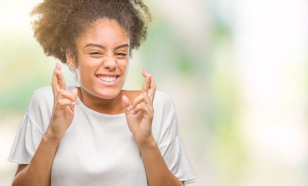 Молодая афро-американка на изолированном фоне улыбается скрещивая пальцы с надеждой и закрытыми глазами. Удача и суеверие
. - Фото, изображение